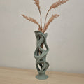 Modern vase with abstract design holding dried plants against a neutral wall.