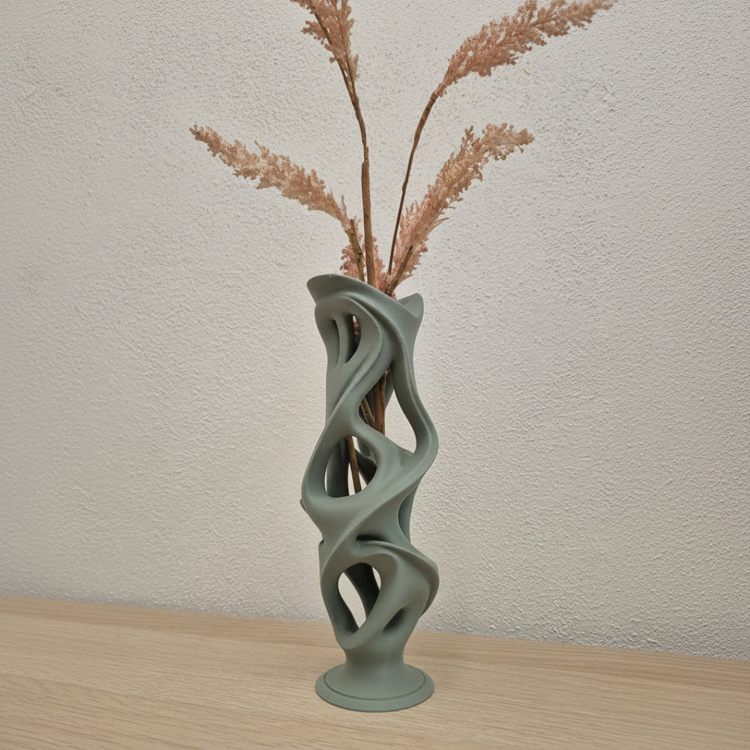 Modern vase with abstract design holding dried plants against a neutral wall.