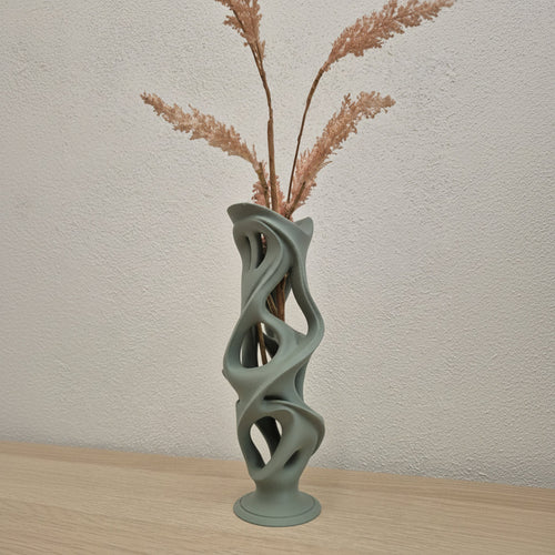 Modern vase with abstract design holding dried plants against a neutral wall.